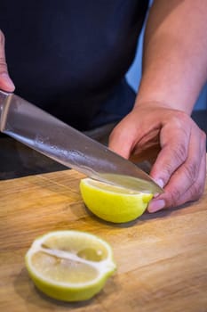 Chef slicing Lemon on wooden cutting board.