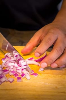 Chef chopping a red onion with a knife on the cutting board.