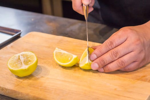 Chef slicing Lemon on wooden cutting board.