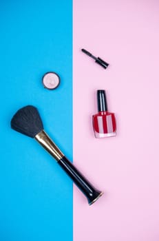 makeup collection with  mascara, nail polish ,eye shadow and brush from above on blue and pink ground