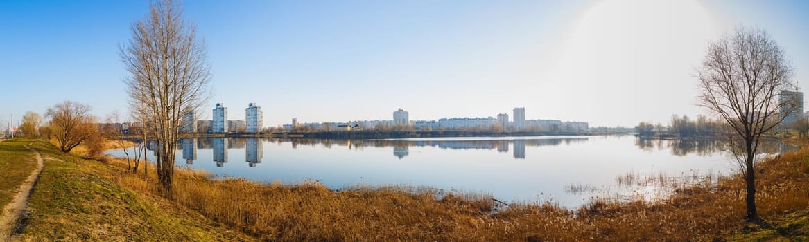 Panoramic shot of large lake. Coastline, the reflection of buildings in calm water.