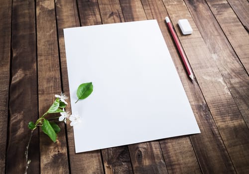 Photo of blank stationery: letterhead, pencil, eraser, cherry flowers and green leaves on wood background. Responsive design mockup.