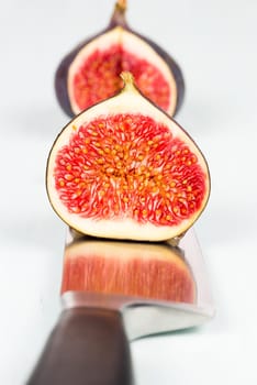 One whole ripe and sweet fig with a cutout is on a kitchen knife with refelction on a light blue vintage background