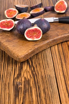 Group of whole and sliced ripe, delicious and sweets figs with a kitchen knife on a old rustic wooden cutting board with copy space in lower picture area
