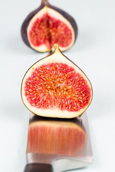 One whole ripe and sweet fig with a cutout is on a kitchen knife with refelction on a light blue vintage background