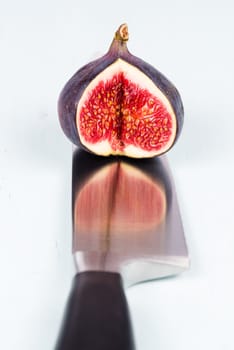 One whole ripe and sweet fig with a cutout is on a kitchen knife with refelction on a light blue vintage background