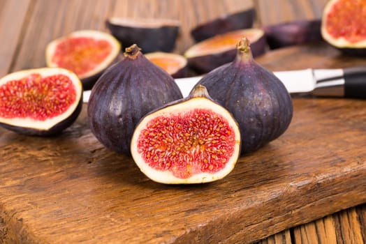Group of whole and sliced ripe, delicious and sweets figs with a kitchen knife on a old rustic wooden cutting board
