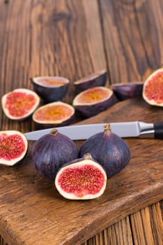 Group of whole and sliced ripe, delicious and sweets figs with a kitchen knife on a old rustic wooden cutting board with copy space in upper picture area
