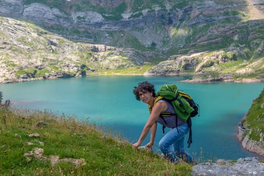 a woman hiker climbs a slope, Lake Estaens in the background