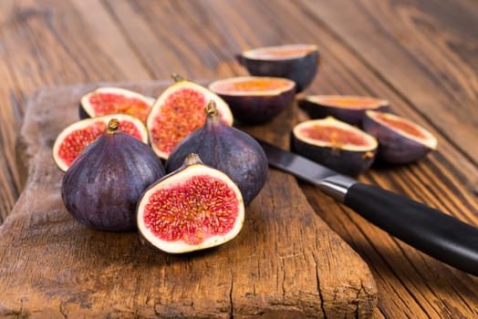 Group of whole and sliced ripe, delicious and sweets figs with a kitchen knife on a old rustic wooden cutting board