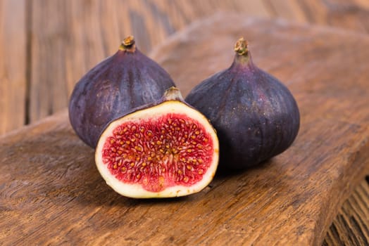 Two whole and one half delicious and sweets figs on a rustic wooden background