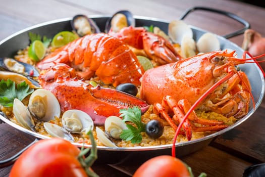 Gourmet seafood Valencia paella with fresh langoustine, clams, mussels and squid on savory saffron rice with peas and lemon slices, close up view