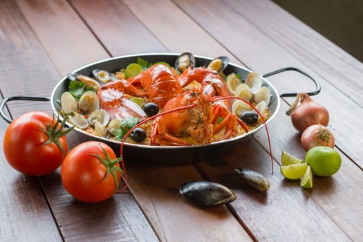 Gourmet seafood Valencia paella with fresh langoustine, clams, mussels and squid on savory saffron rice with peas and lemon slices, close up view
