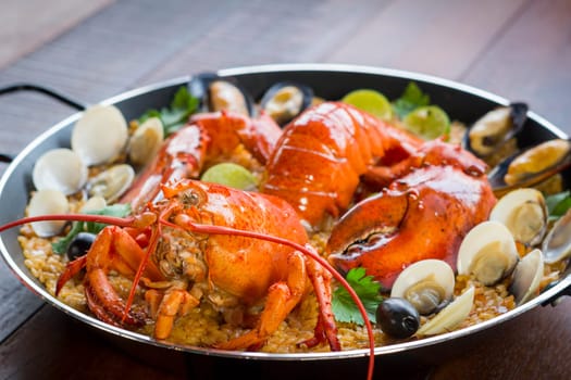 Gourmet seafood Valencia paella with fresh langoustine, clams, mussels and squid on savory saffron rice with peas and lemon slices, close up view