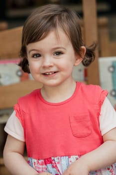 Front view of a little girl standing with curiosty in her face looking at the camera. Smiling for a headshot.