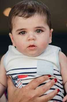 Headshot of a baby boy being held by an unrecognisable person for a headshot indoors.
