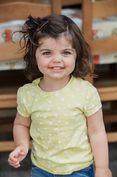 Front view of a little girl standing indoors, looking at the camera and smiling for a headshot. The little girl is wearing casual clothing.