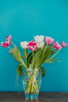 Vase of tulips on top of a side table. The colourful flowers are infront of a bold coloured teal wall.