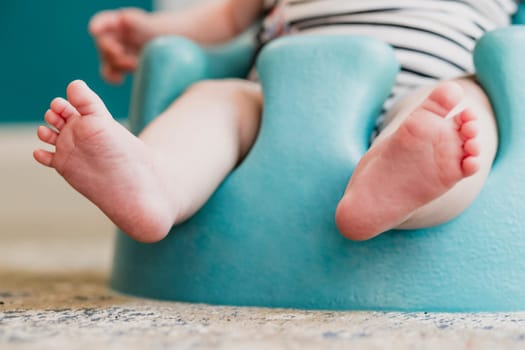 Low angle front view of a unrecognisable baby. The baby is sitting in a floor seat, the focus is on the babies feet.