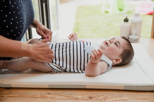 Side view of a baby boy lying on his back. The little boy is getting his nappy changed by his mother who is unrecognisable.