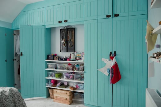Wide angle view of a bedroom interior with a wardrobe and door partially open. There is also storage space and shelves in the middle between the two built in wardrobes.