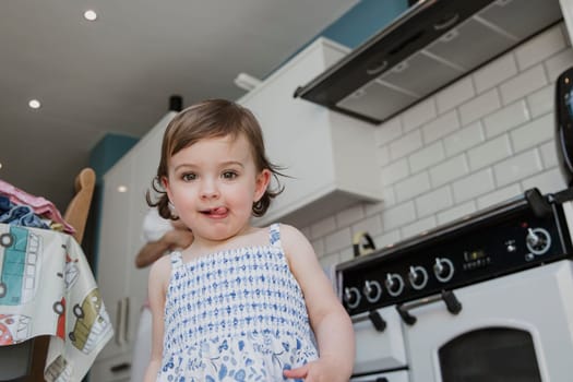 Low nagle view of a little girl looking at the camera. She is stood in the kitchen and pulling a cheeky facial expression with her tongue sticking out.