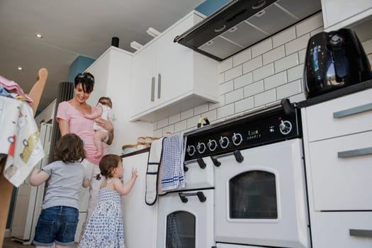 Low angle view of a mother with her three daughters standing in the kitchen. Two of the little girls are stood trying to get the attention of their mother.