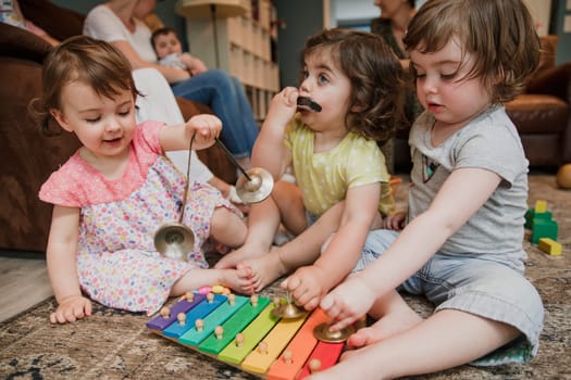 Three little girls sitting in on the floor in a living room playing together and having fun. They are each playing different musical instruments  symbols, xylophone and harmonica.