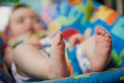 Unrecognisable baby relaxing in a baby bouncer. Focus on the foreground on the babys feet. The background of the image is out of focus.