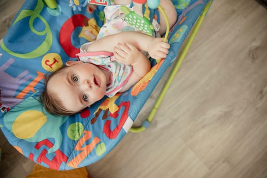 High angle view looking down onto a baby girl relaxing in her baby bouncer. The baby is looking up into the camera and smiling.