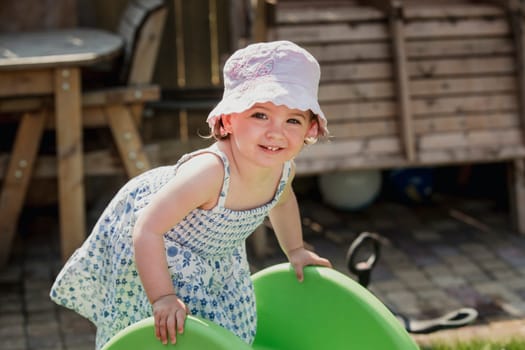 Front view of a little girl looking at the camera. The little girl is climbing up the plastic slide in the back garden and having fun.