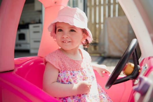 One little girl sitting outside in her toy car using her imagination. She is looking out of the window, smiling and enjoying herself.