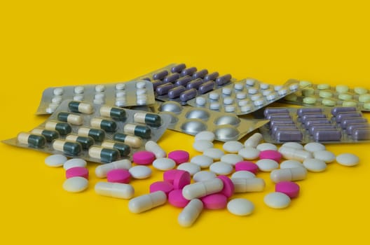 On a yellow background white and pink tablets and blisters with colorful pills are scattered. Side view.