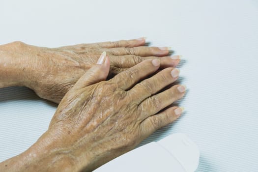hand of senior woman with lotion bottle on white table background.