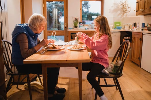 Side view of a grandmother and her granddaughter sitting at the dining table. They are both eating their meal.