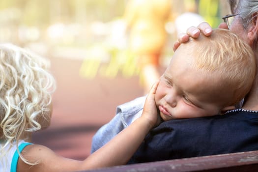 Grandmother and sister hugging and comfort the upset kid in the playground