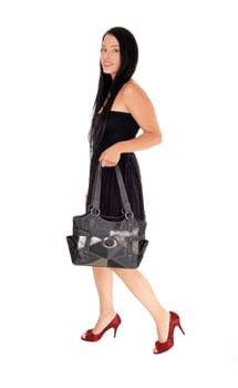 A beautiful woman walking in a black dress holding her handbag.and in red heels and long black hair, isolated for white background.