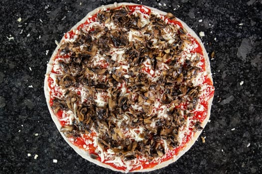 Pizza with mushrooms on black table, ready to be put in the oven to be baked