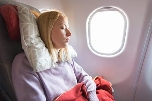 Tired blonde casual caucasian woman sleeping on seat while traveling by airplane on long distance transatlantic flight. Commercial transportation by planes.