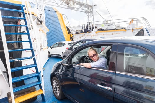 Female driver parking her car on ferry boat on trip to their summer vacations island destination. Sardinia, Italy. Water transport concept.
