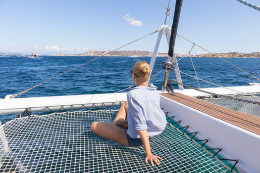 Casual woman relaxing on a summer vacations sailin cruise, sitting on a luxury catamaran, sailing in Maddalena Archipelago, Sardinia, Italy.