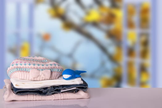 Stack colorful girl clothes. Pile of girl clothes with a funny toy whale on a bright table in front of blurred natural autumn background. Space for your display product montage. Autumn fashion.