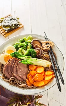 Plate of traditional Japanese Gomoku Yakisoba, or stewed pork, sliced and served with fresh vegetables and black spaghetti on a rustic plate with copy space