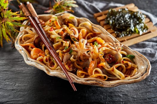 Japanese seafood appetizer with fried noodles, clams, shellfish, shrimp, squid and calamari served in a large shell with nori on the side