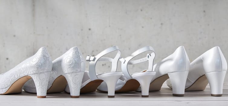 Line of three pairs of stylish white high heel shoes viewed from the back with the center pair having straps in a concept of wedding fashion with copy space above in panorama view