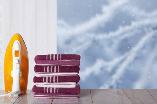 Closeup of yellow iron and a stack striped towels on rustic table in front of window with blurred winter landscape. Template for your display product montage. Space.