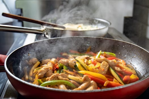 Chicken and vegetables fried in red pan on the hob