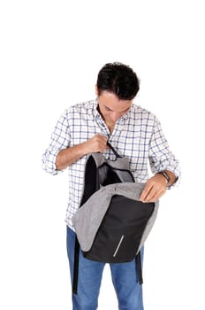 A handsome young man standing from the front looking into his open.backpack, isolated for white background.