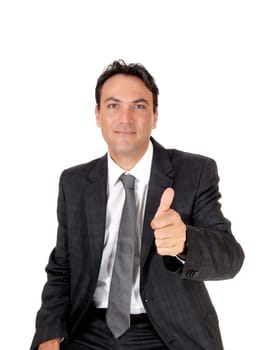 A young business man sitting in a dark gray suit and tie showing his.approval with his thump up, isolated for white background.