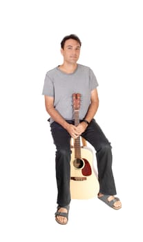 A young handsome man taking a brake from playing the guitar, sitting.in jeans gray shirt and sandals, isolated for white background.